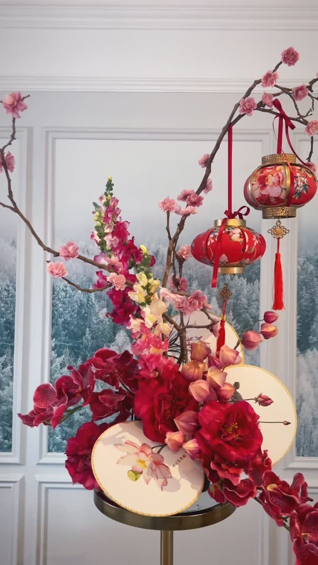 Red and pink floral arrangement with Chinese lanterns on a gold stand.