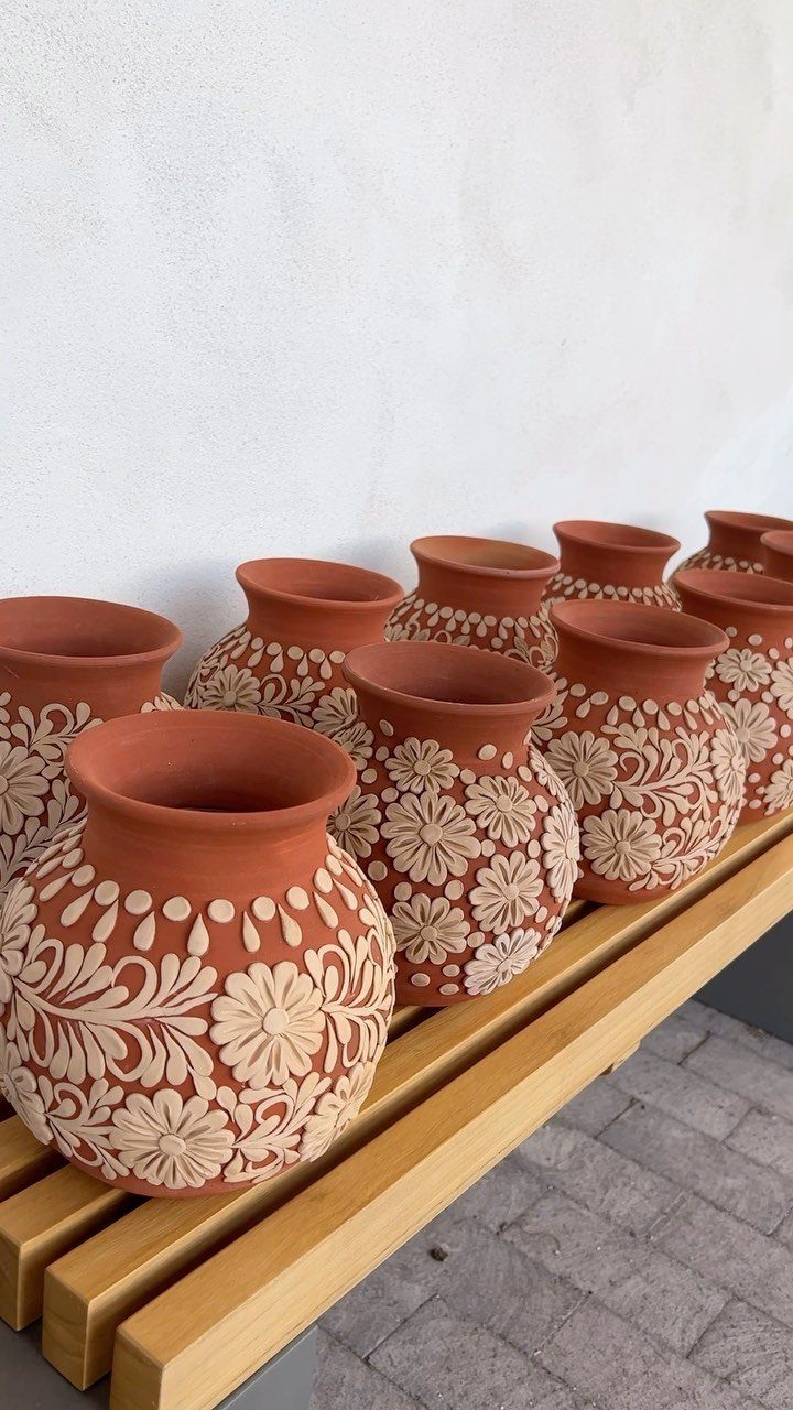 Terracotta clay pots with white floral carvings arranged on a wooden slatted shelf.