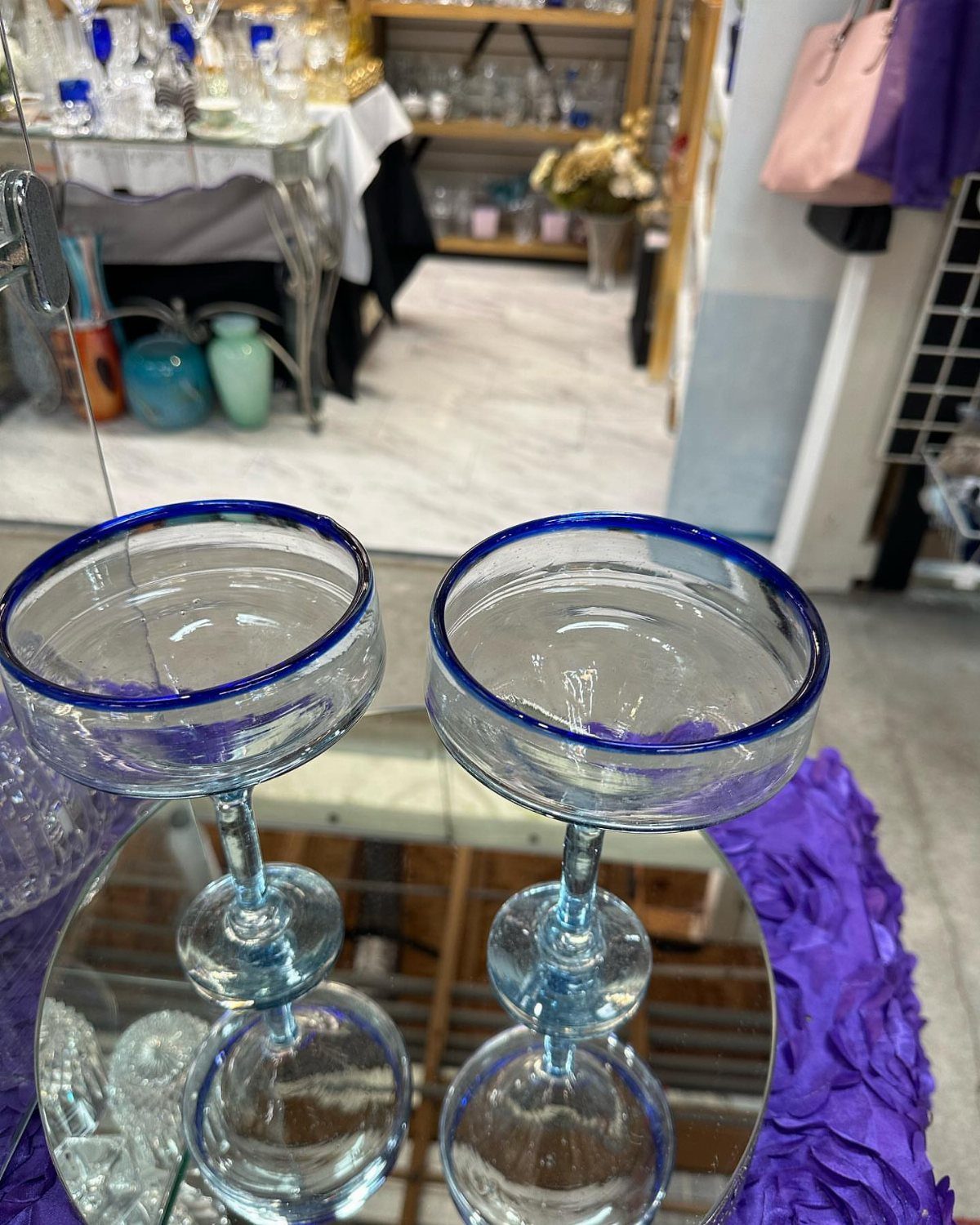Two clear margarita glasses with blue rims on a mirrored surface.