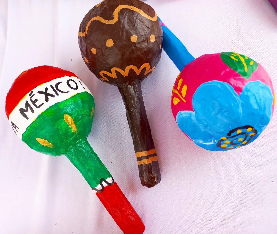 Three colorful handmade maracas with Mexican flag and floral designs on white fabric.