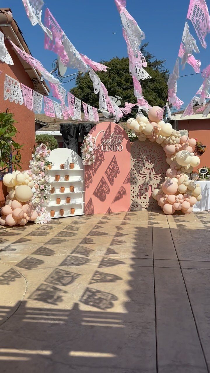 Pink and white papel picado banners hanging over an outdoor party decoration setup.