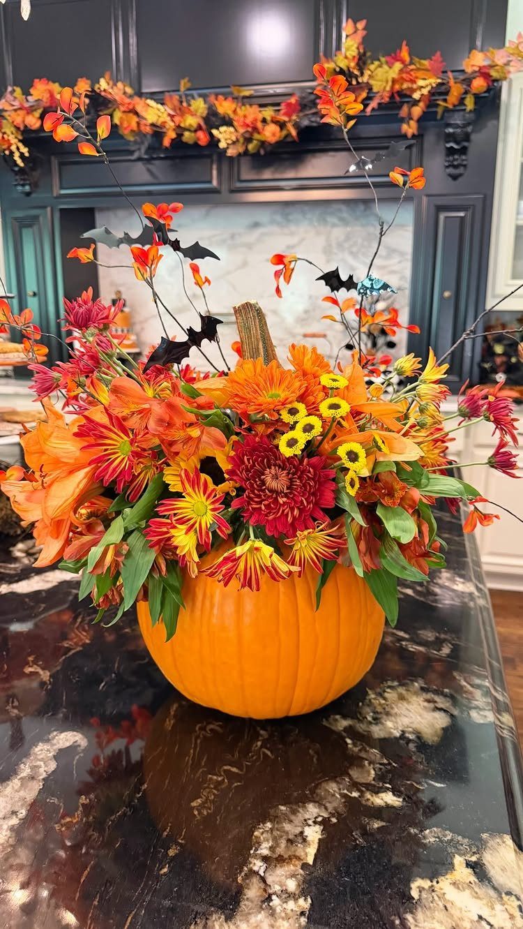 Orange pumpkin vase filled with clustered autumn flowers on a dark marble counter.