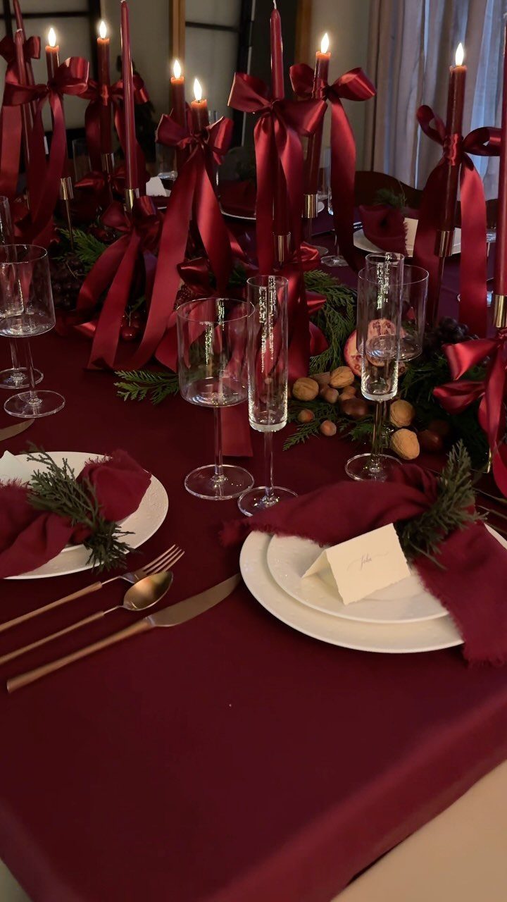 Burgundy table setting with gold silverware, white plates, and tall ribboned candles.