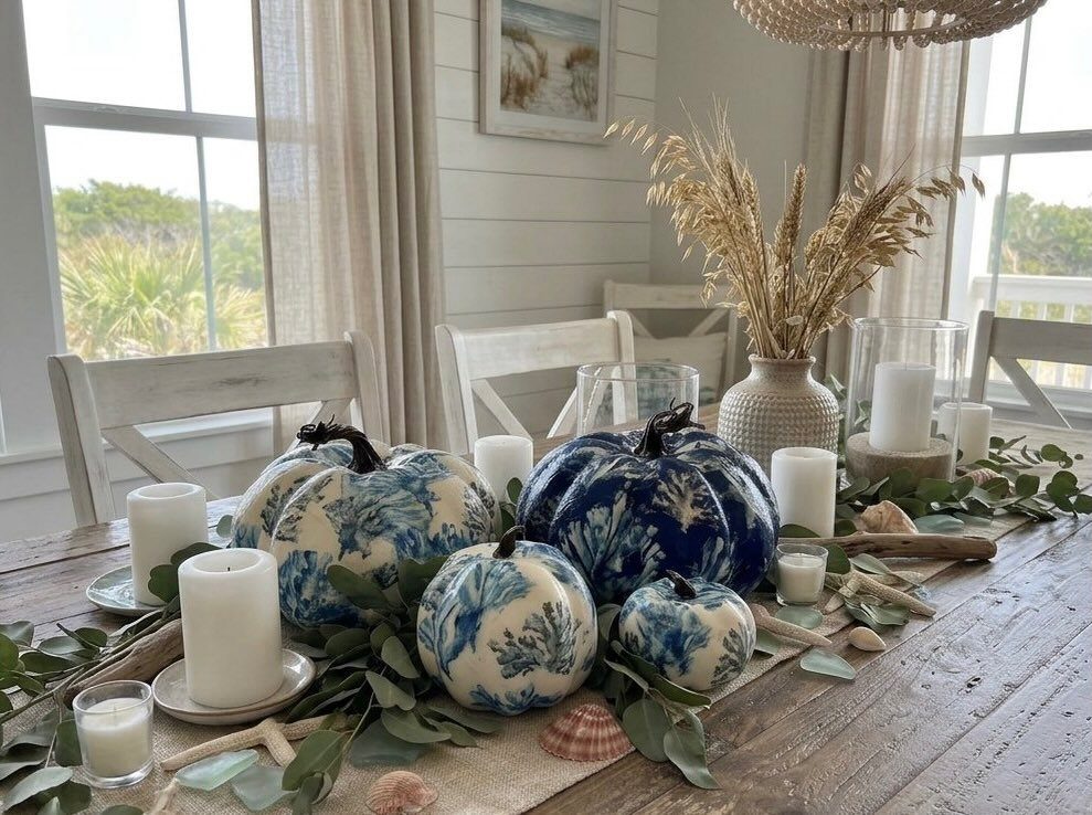 Blue and white patterned pumpkins with seashells and candles on a wooden table.