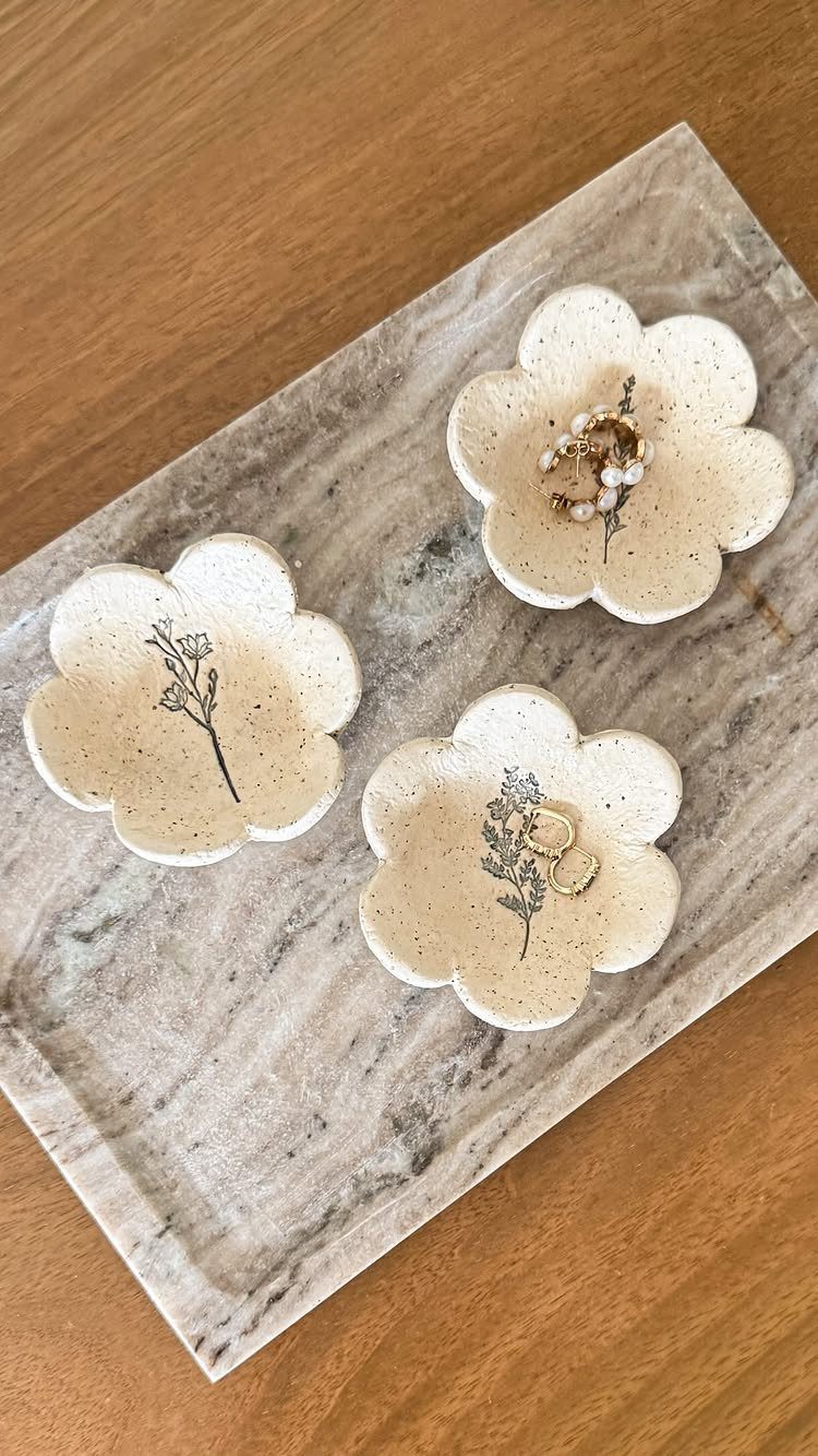Three flower-shaped clay dishes with botanical drawings on a marble tray.
