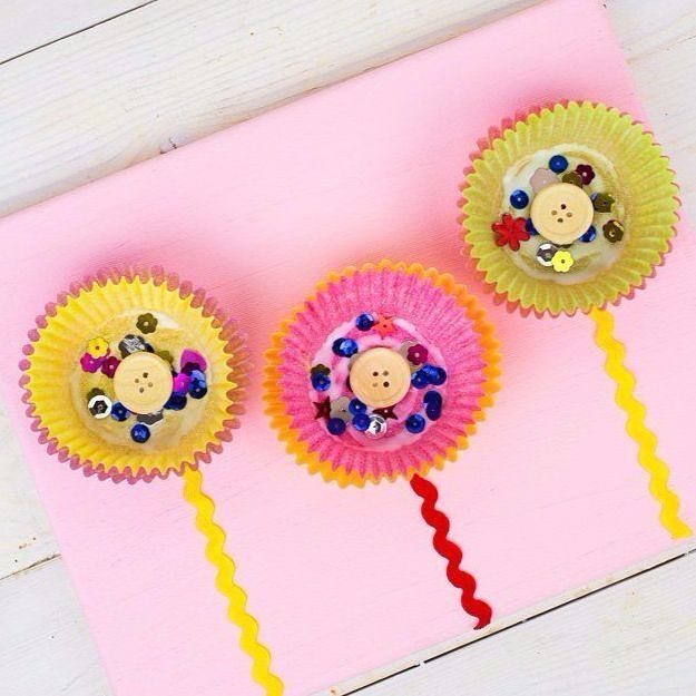 Colorful craft flowers made from cupcake liners and buttons on a pink background