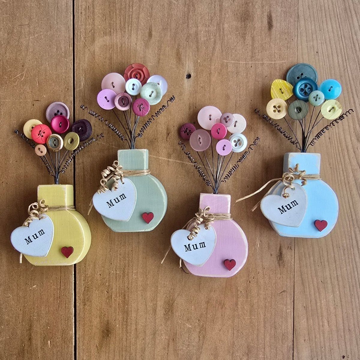 Four colorful wooden vase crafts with button flowers and heart tags saying Mum.