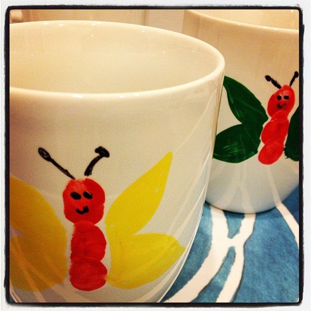 Hand-painted white ceramic mugs with colorful butterflies on a blue patterned background