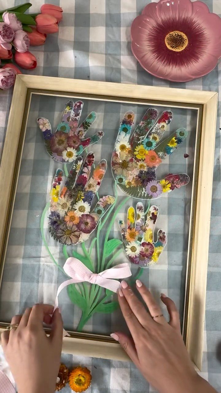 Pressed flower art in handprint shapes arranged as a bouquet in a frame.