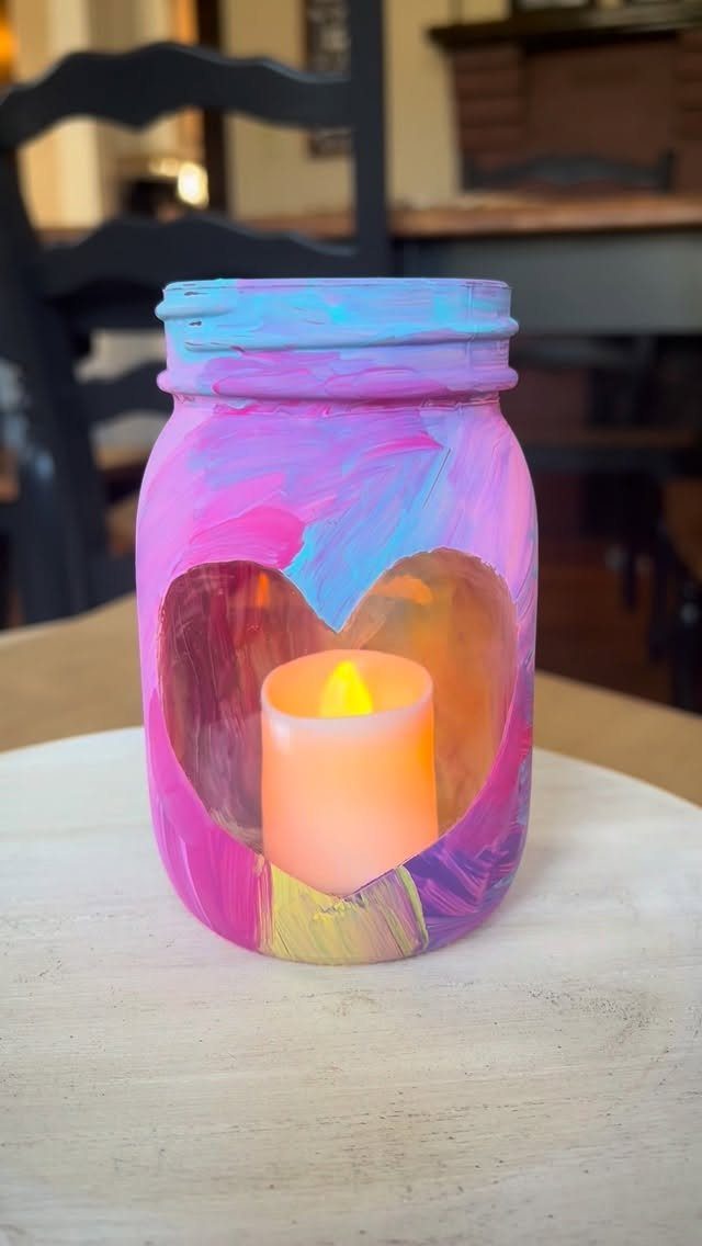 Painted mason jar votive with a heart cutout and a glowing candle inside.