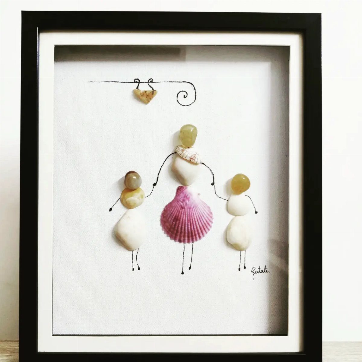 Seashell and pebble art depicting a mother and two children holding hands.