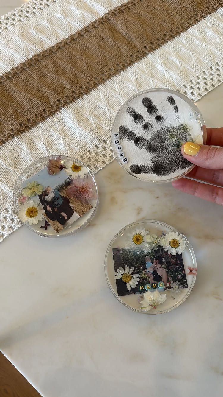 Three clear resin coasters with a handprint, dried flowers, and a photograph.