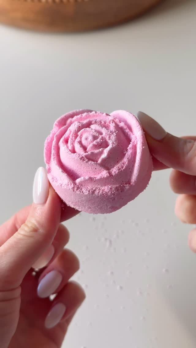 Pink rose-shaped bath bomb held by two hands with white nail polish.