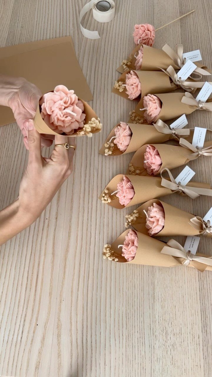 Pink flower-shaped candles wrapped in brown paper and tied with ribbons on wood.