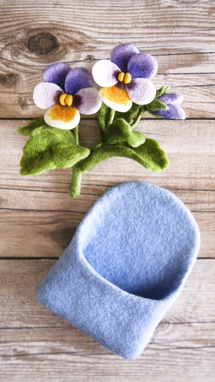 Purple and yellow felt pansies with green leaves on a wooden background.
