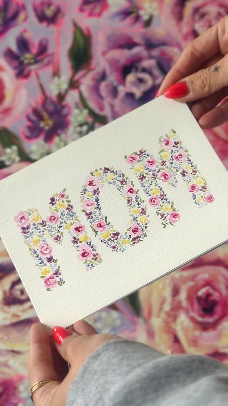 White card with floral MOM lettering held by hands over purple floral fabric