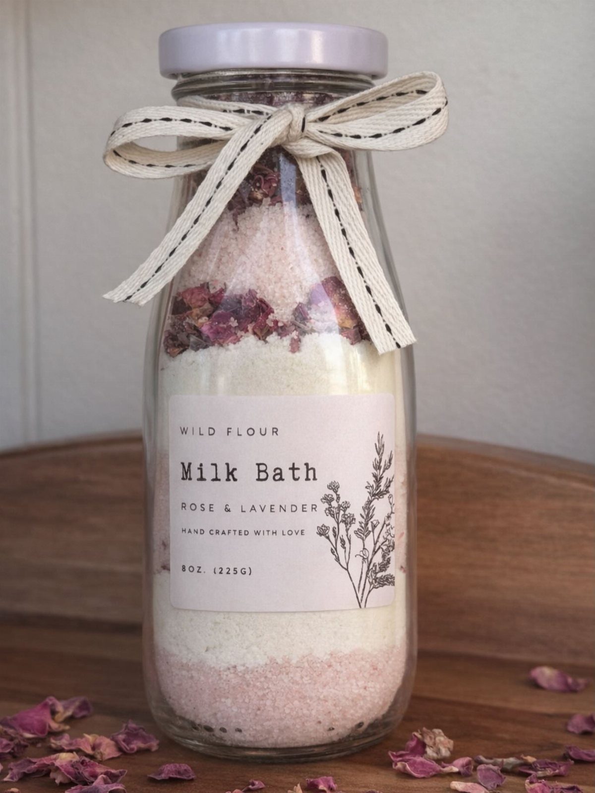 Glass bottle of layered floral milk bath salts tied with a cream bow.