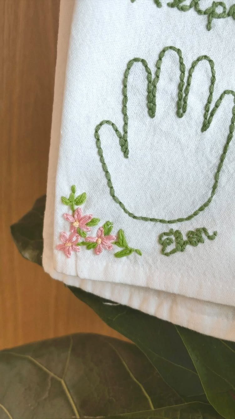 White dish towel with a green embroidered handprint and small pink flowers.
