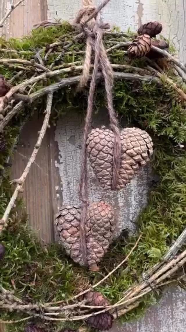 Rustic mossy wreath with two hanging pinecone hearts on a weathered wooden wall