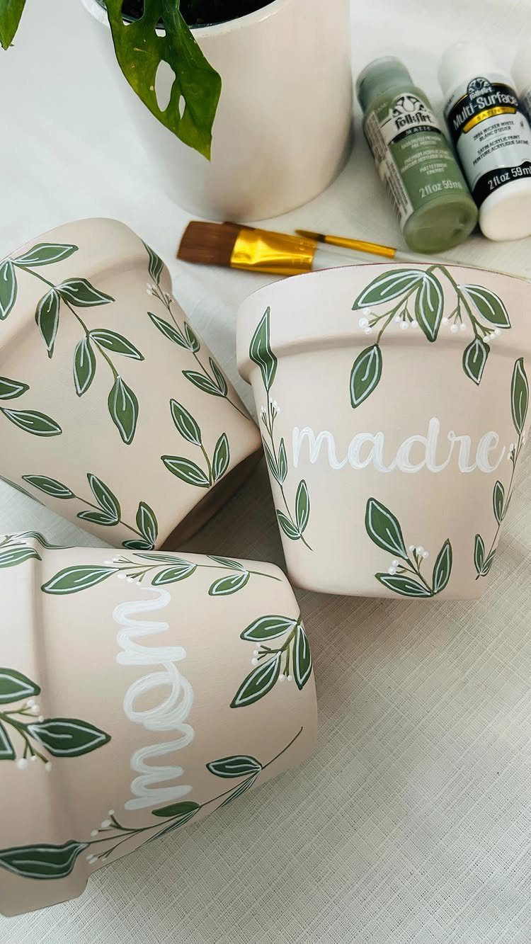 Painted terra-cotta pots with green leaf designs and the words mom and madre.