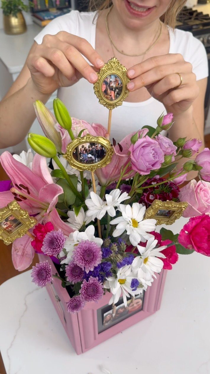 Person holding a small gold-framed photo in a pink floral arrangement box