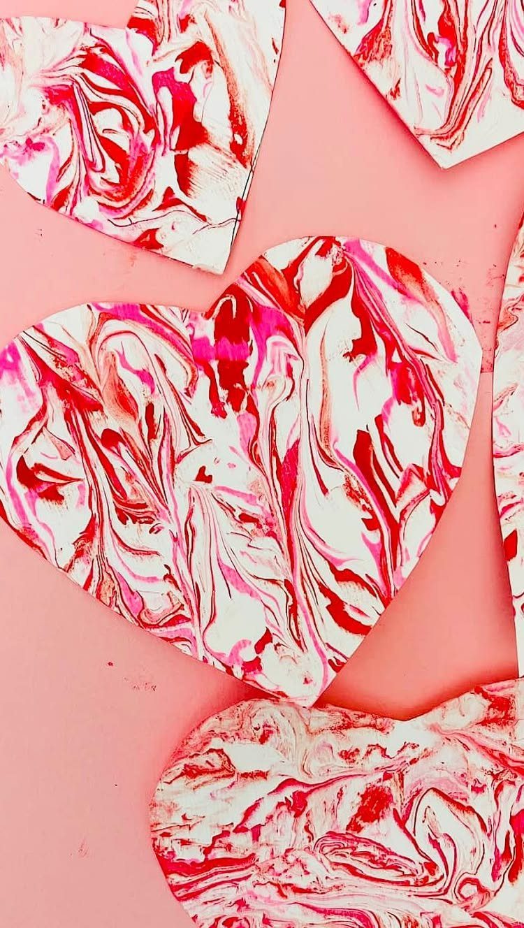 Heart-shaped paper cutouts with red and pink marbled paint on pink background