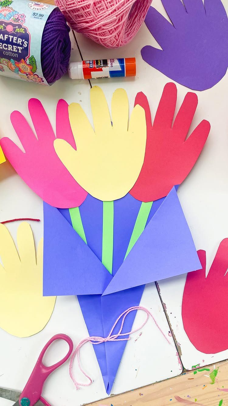 Paper bouquet made from colorful handprint cutouts wrapped in purple paper with craft supplies.