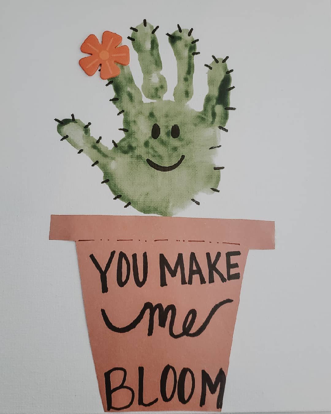 Green handprint cactus with a smiley face and pink paper pot on white paper.