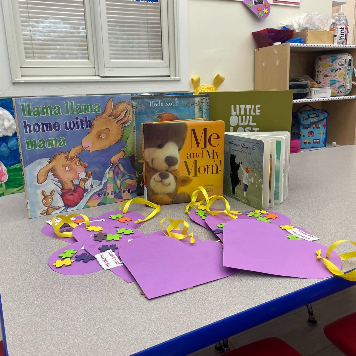 Purple heart paper crafts with yellow ribbons and children's books on a table.