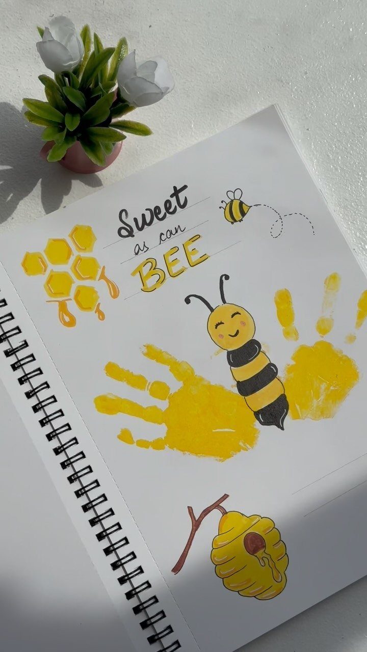 Yellow handprints on a notebook page transformed into a bee with drawings.