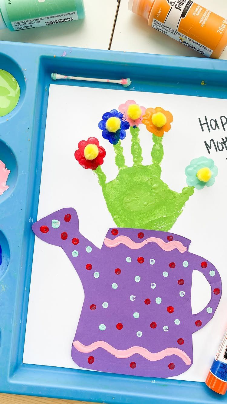 Green handprint flower craft emerging from a purple paper watering can on white paper.