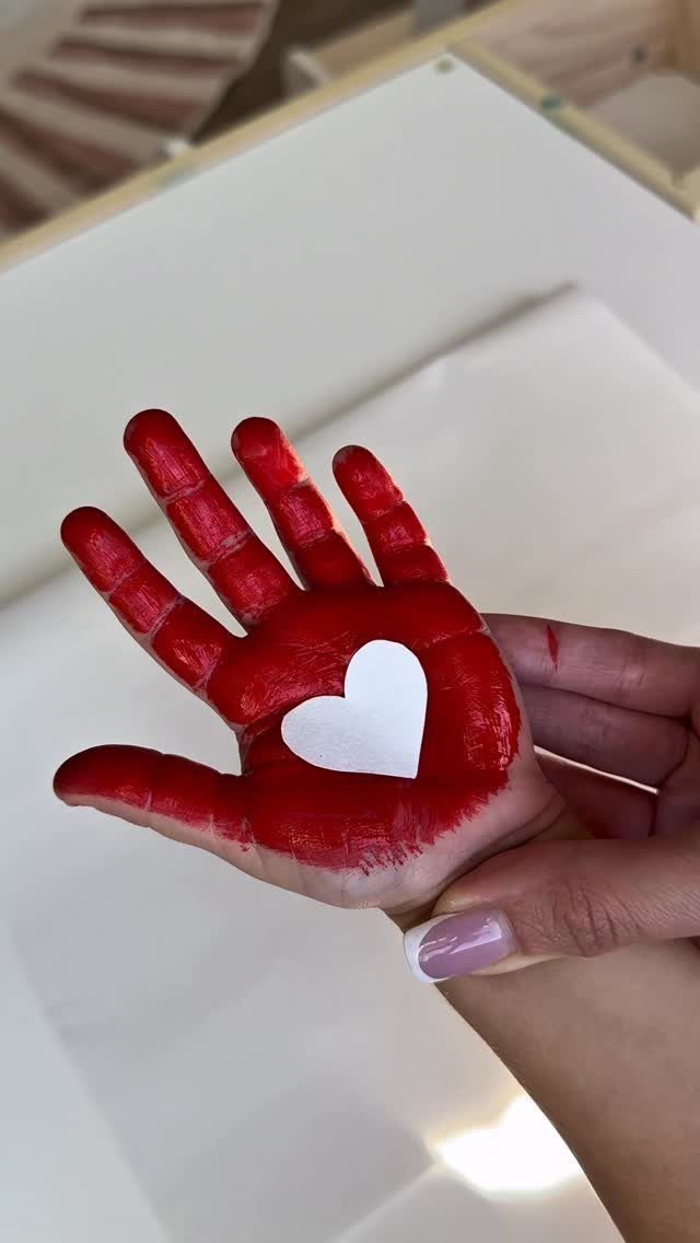 Child's hand painted red with a small white paper heart on the palm.