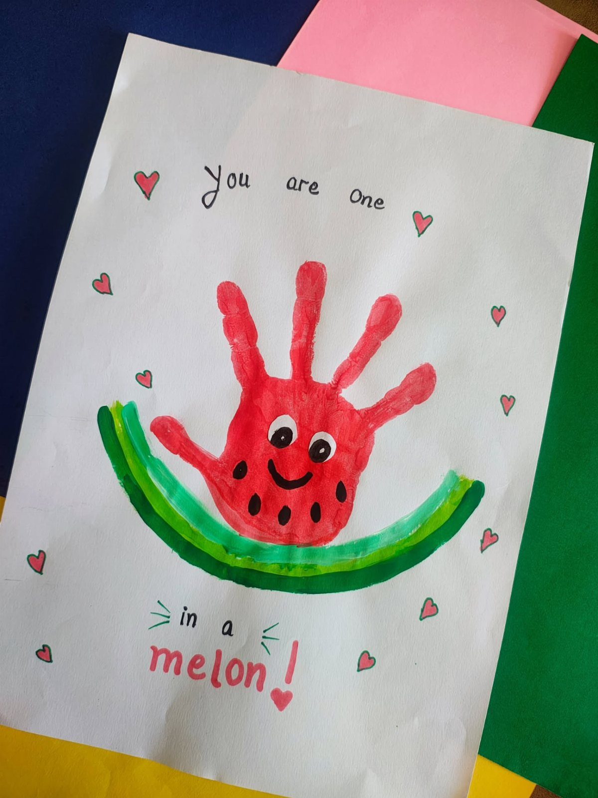 Red paint handprint watermelon art on white paper with handwritten Mother's Day message.