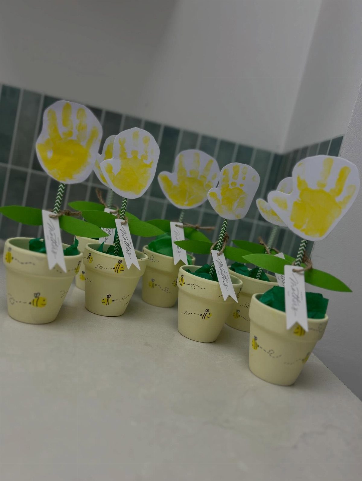 Handprint paper flowers in small cream pots with green stems and white tags.