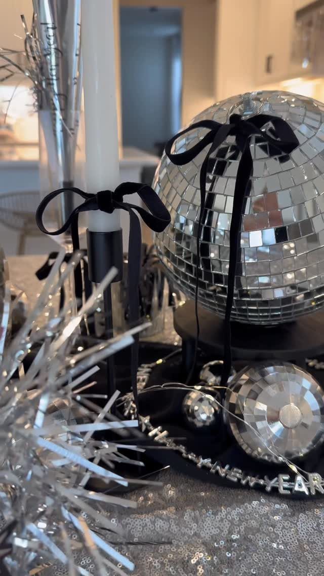 Mirrored disco ball with black ribbon bow among silver New Year's Eve decorations.