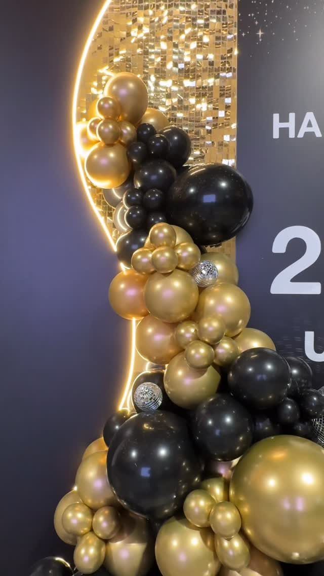 Gold and black balloon cluster against a dark background with shimmering gold accents.