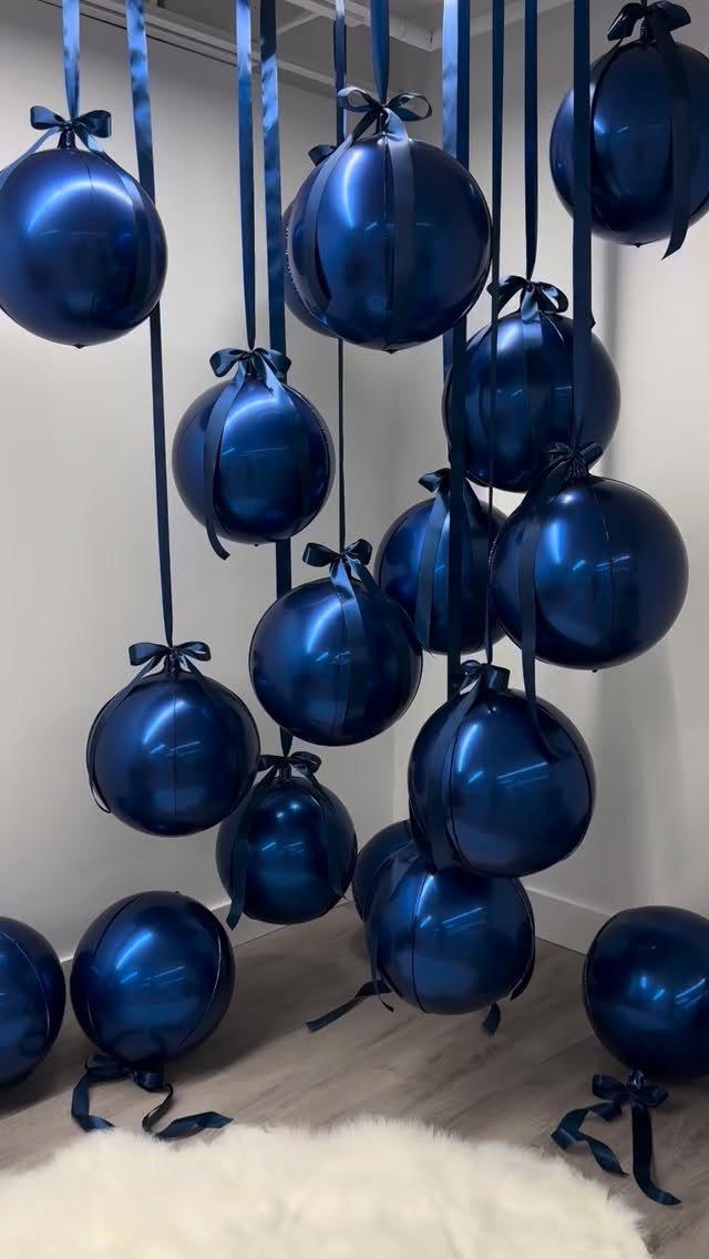 Dark blue metallic ornaments hanging from ribbons against a white wall