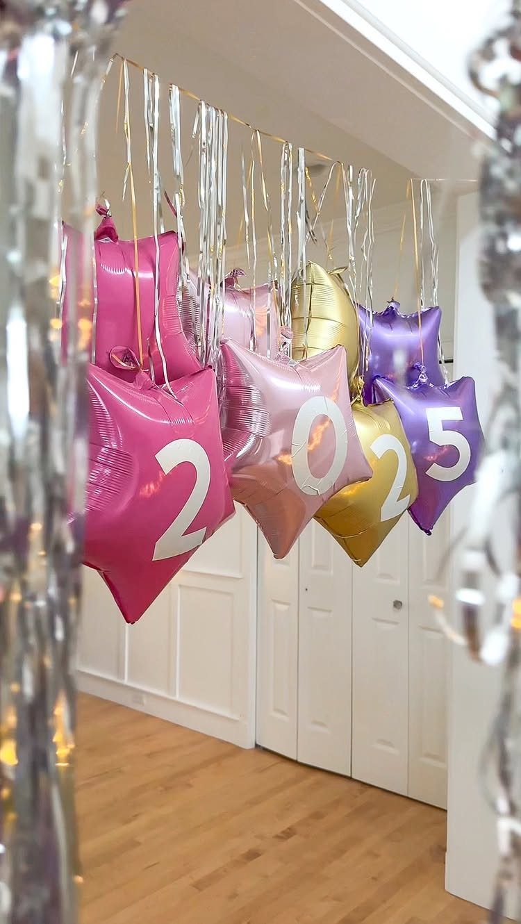Star-shaped foil balloons spelling 2025 hanging from a ceiling with silver tinsel garlands.