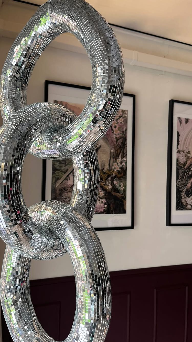 Interlocking silver mirrored rings hanging as a decorative installation against a white wall.
