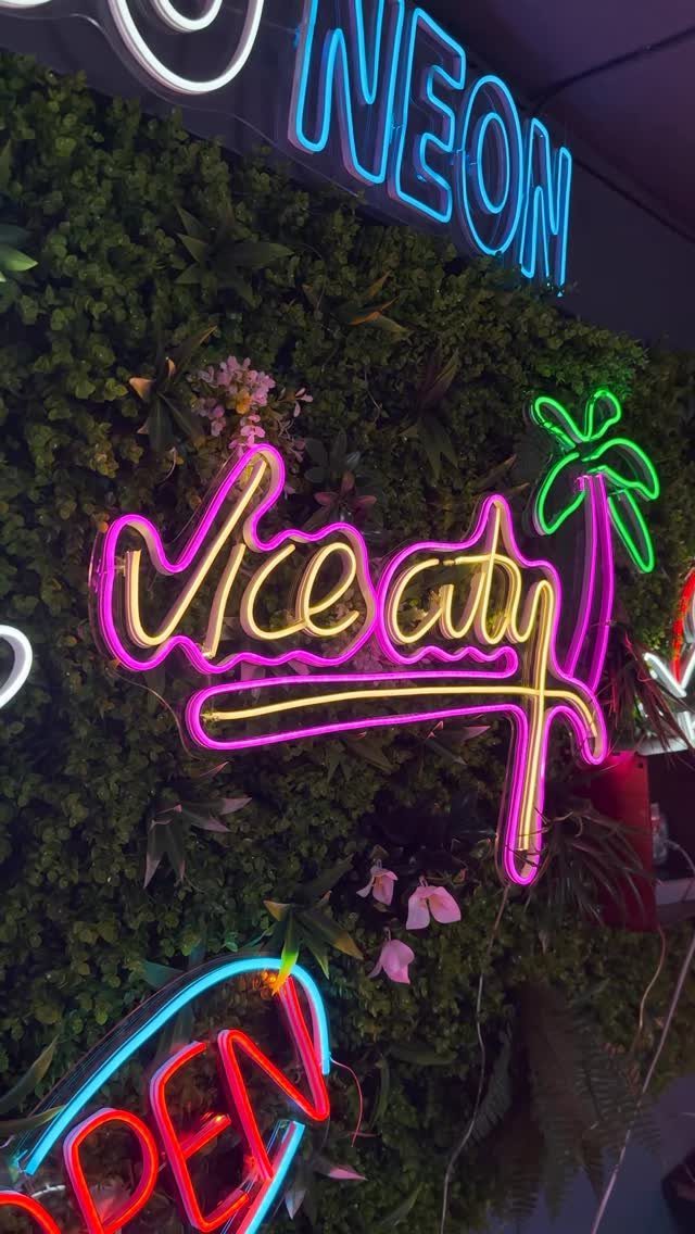 Colorful neon signs on a green hedge wall, including a pink Vice City sign.