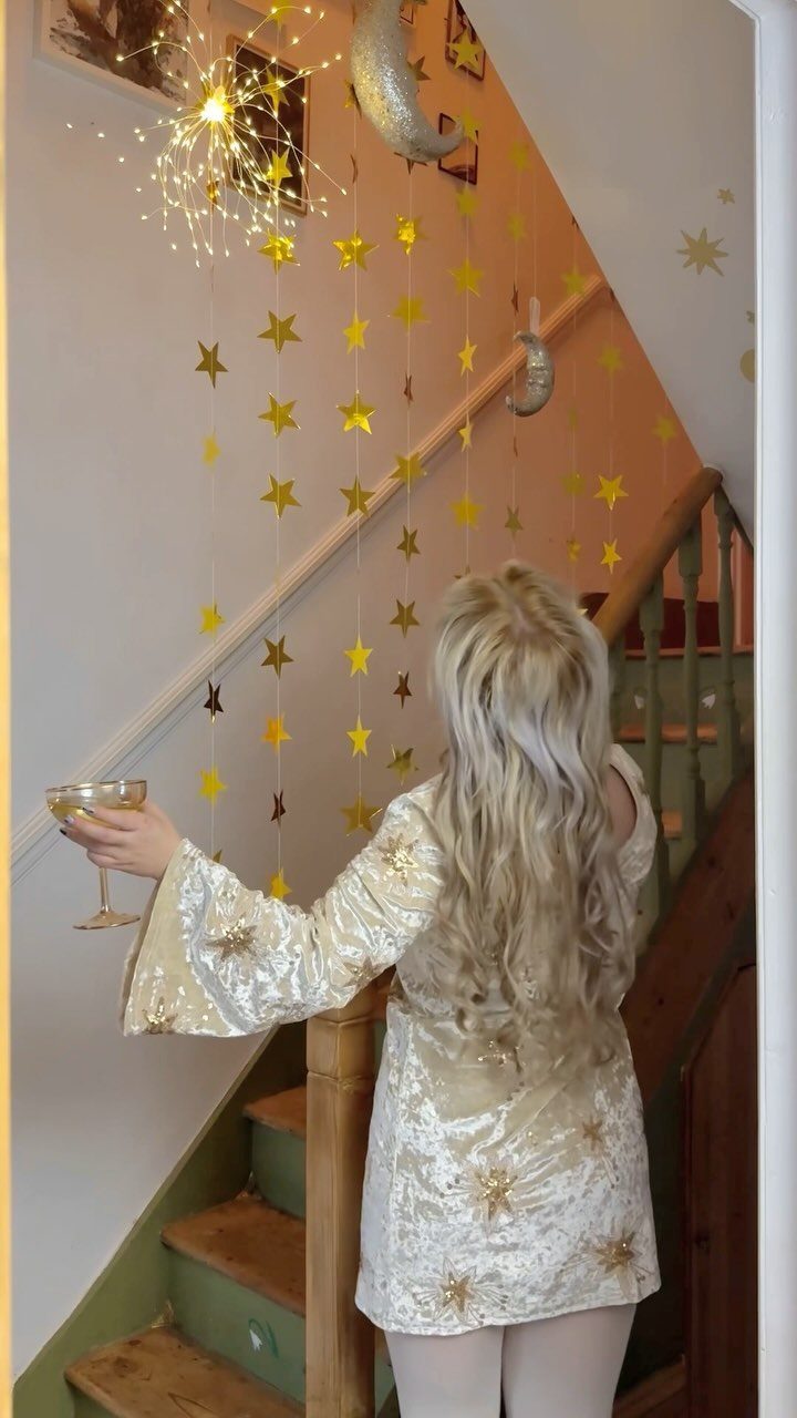 Woman in gold dress by staircase decorated with gold stars and fairy lights