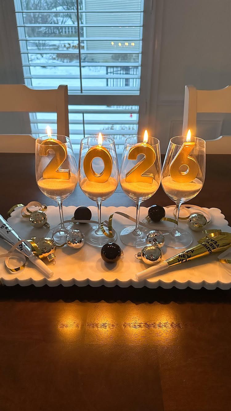 Gold number candles 2026 in wine glasses with ornaments on a white tray