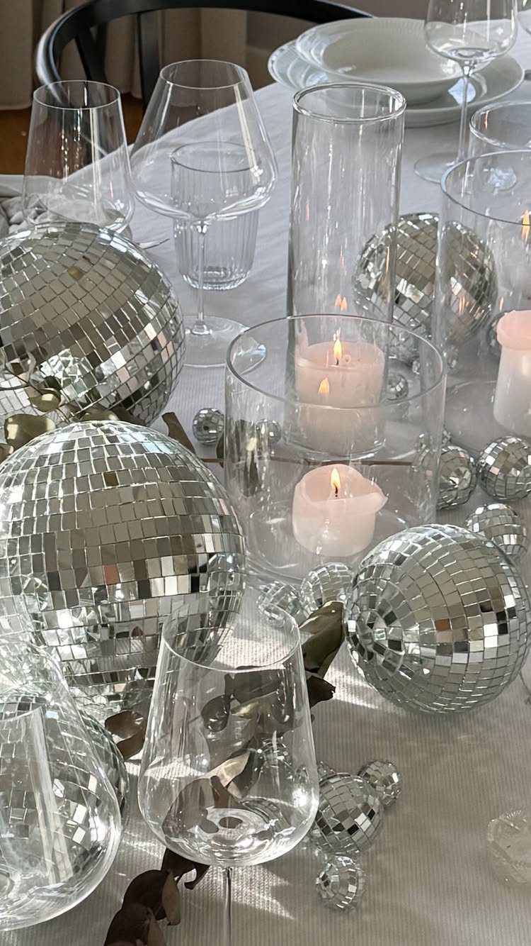 Disco balls and lit candles decorating a white table with clear glassware.