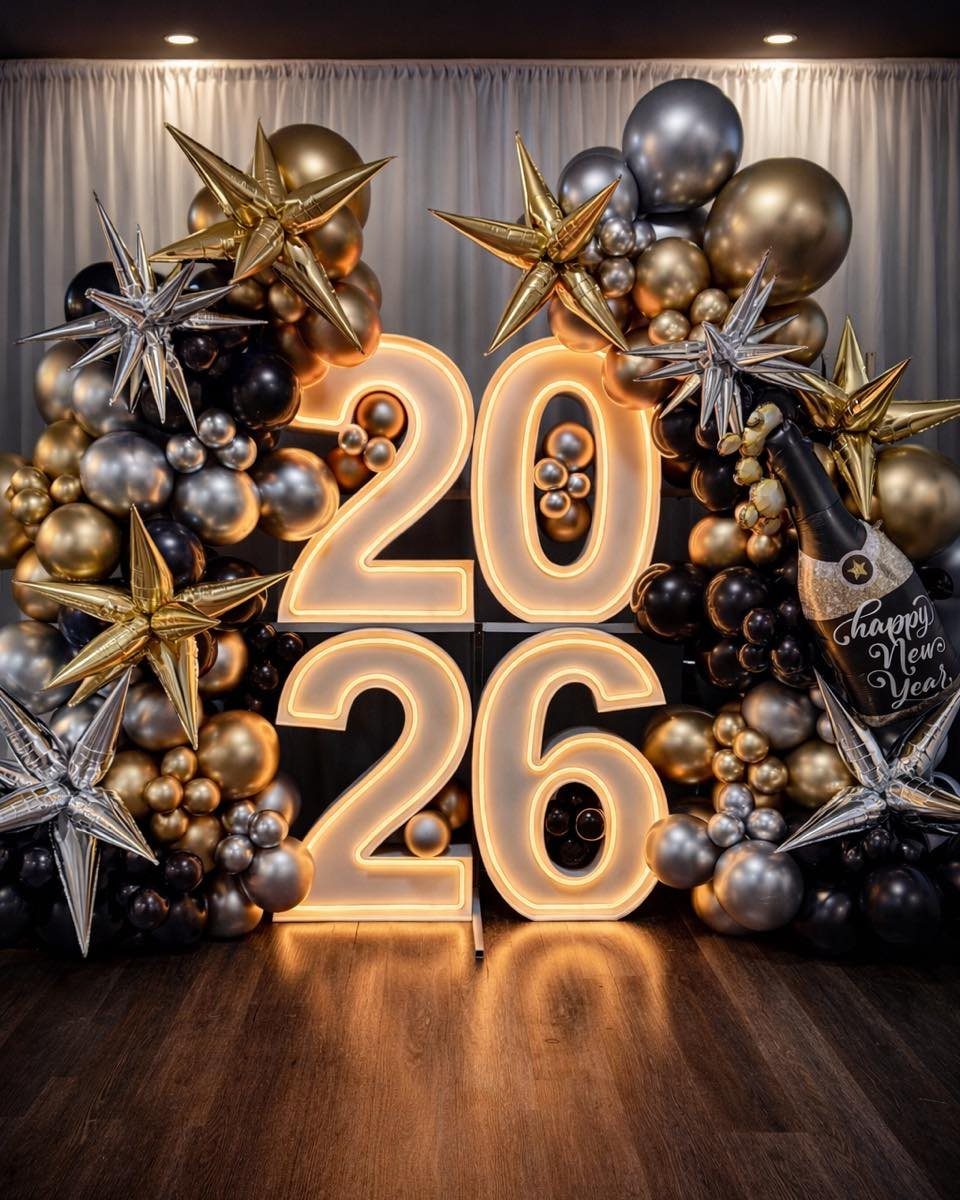 Glowing 2026 numbers surrounded by gold and silver balloons and metallic stars.