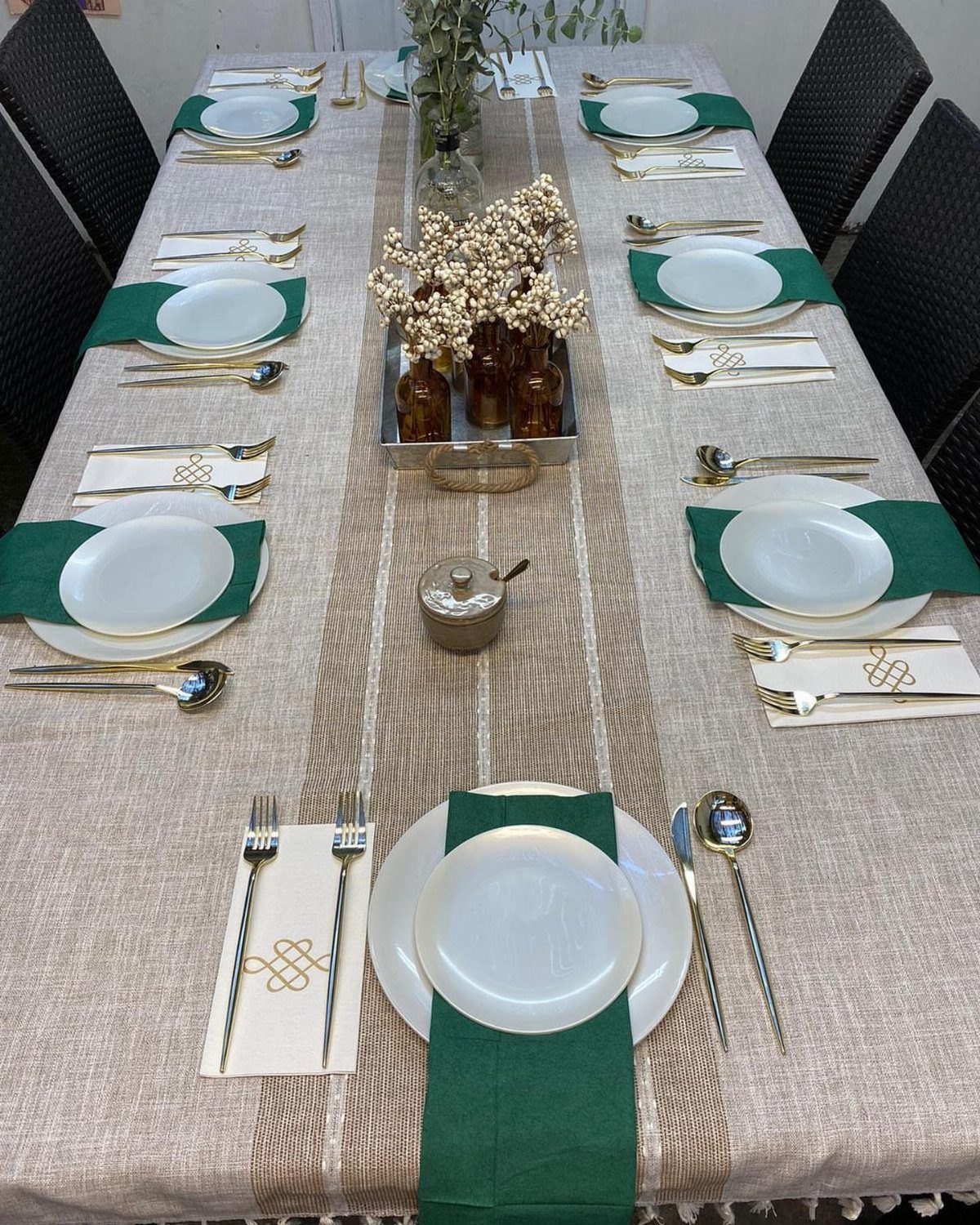 Elegant table setting with white plates, green napkins, and gold cutlery on beige linen.