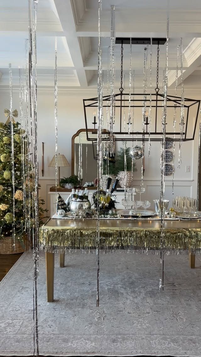 Gold table with tinsel skirt surrounded by hanging silver tinsel curtains in a room.