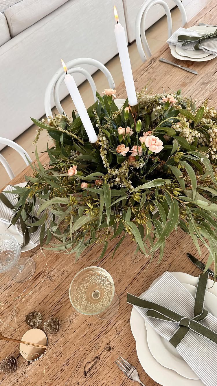 Green foliage and pink flower centerpiece with white candles on a wooden table