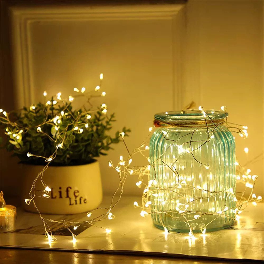 Blue glass jar and potted plant illuminated by warm white fairy lights.