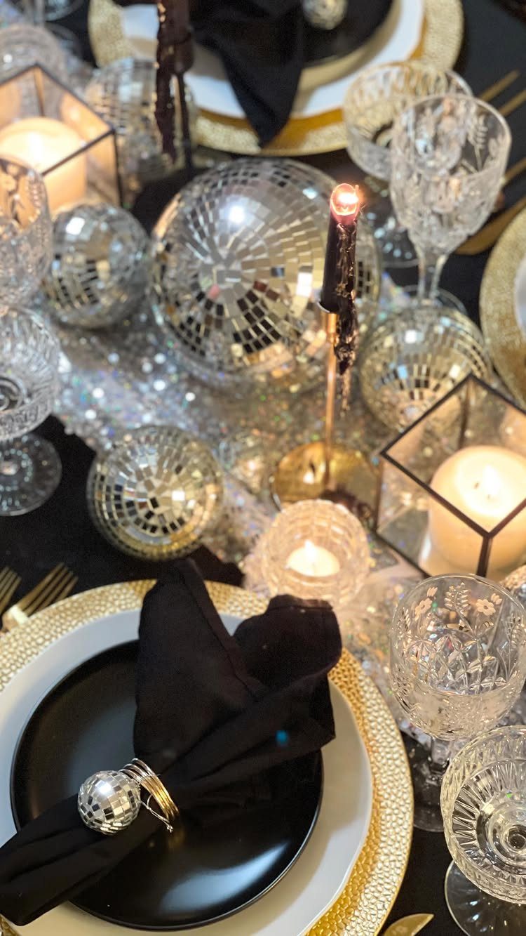 Black plates and gold chargers decorated with disco balls and lit candles.