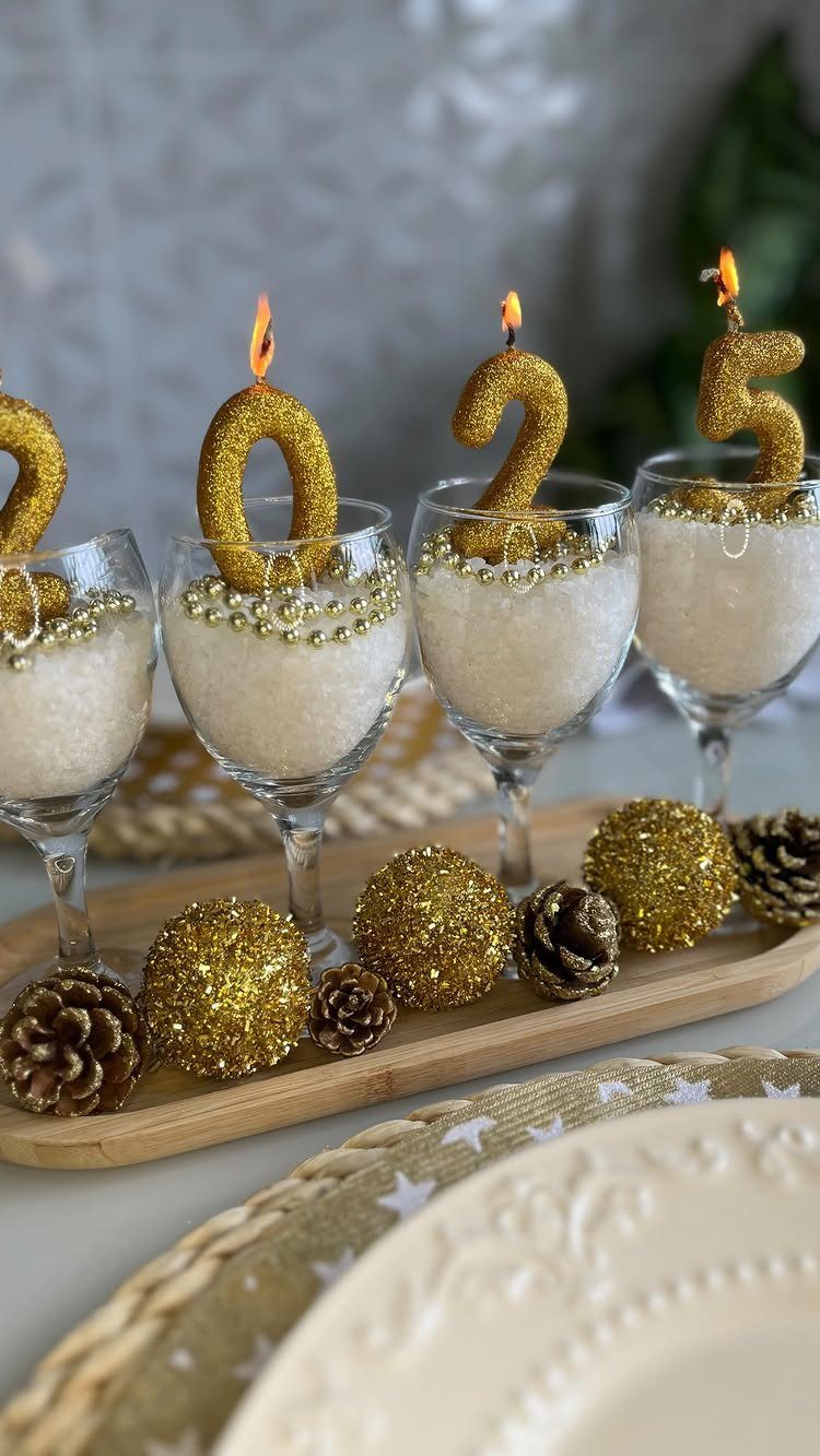 Gold glittery 2025 number candles atop champagne glasses on a decorated wooden tray.